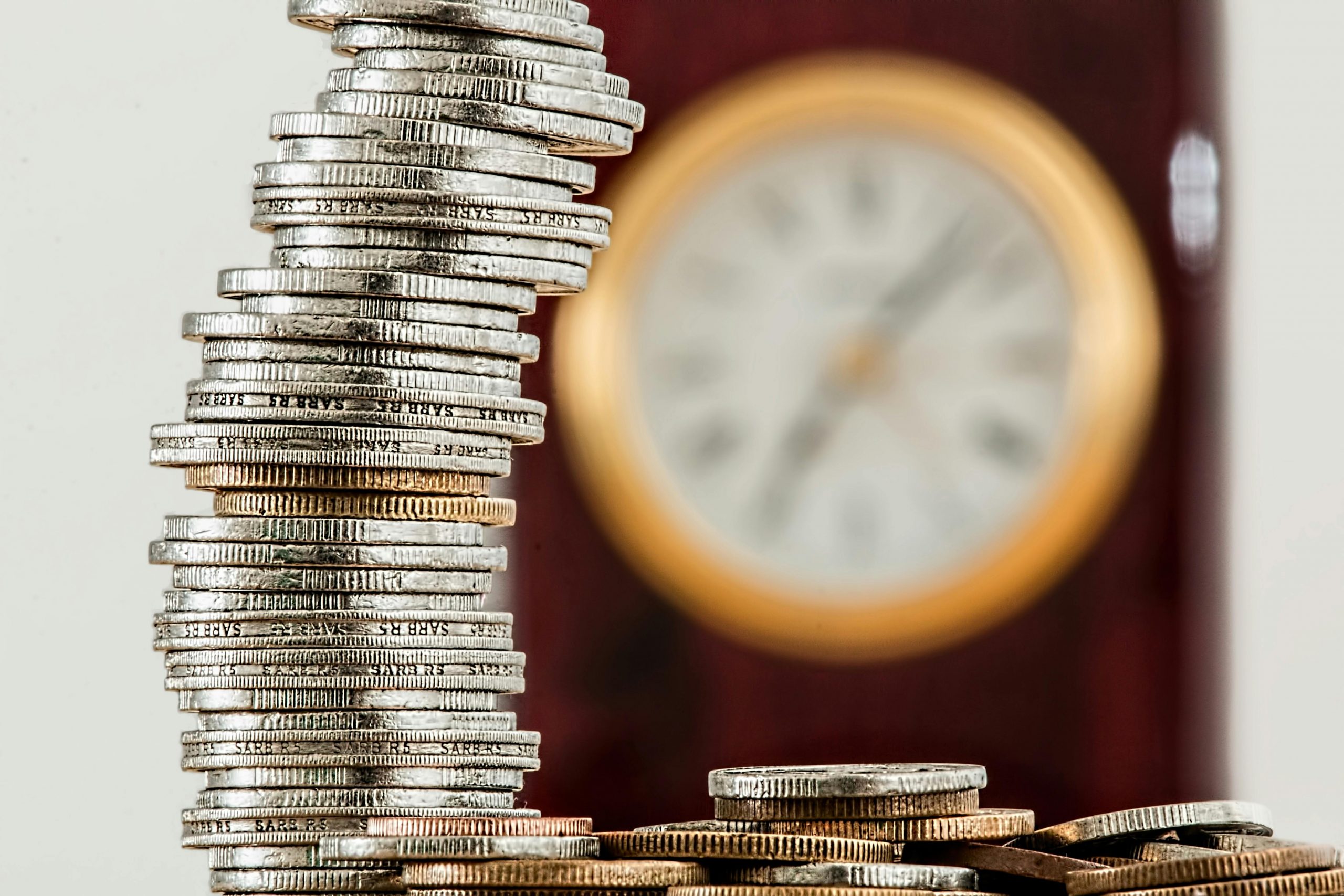stacked coins on a desk with a clock hanging on the wall in the background